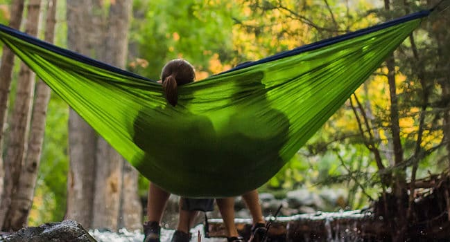 two people in a green hammock seen from the back against a forest of trees. On our quest to manage stress, nature, other people, and time to truly relax can be powerful tools.