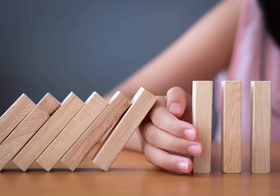 Girl's hand Stopping Falling wooden Dominoes effect from continuous toppled or risk, strategy and successful intervention concept for business and education.